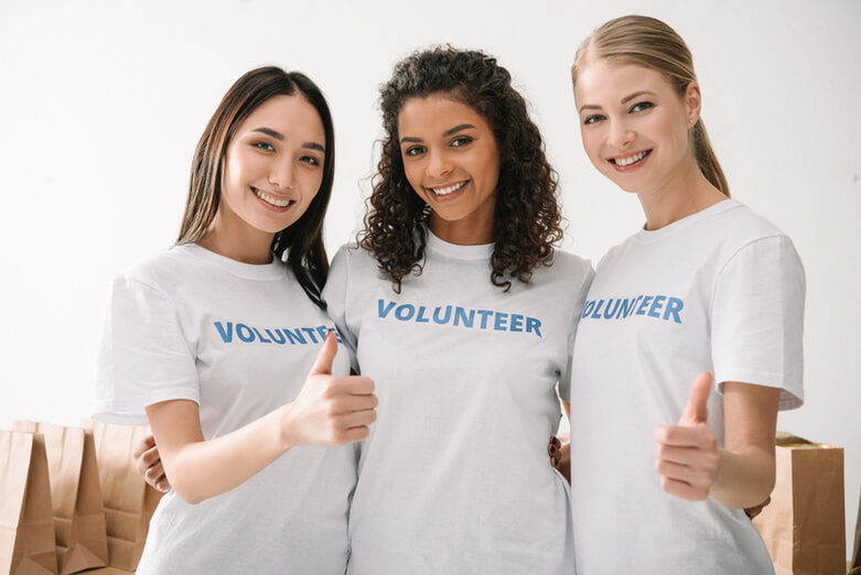 Three young women volunteers standing together and smiling at the camera.]