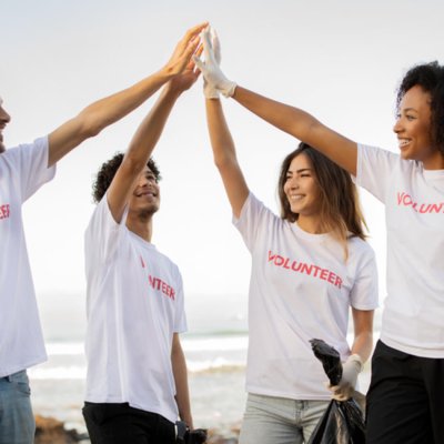 Four volunteers high-fiving on a beach holding trash bags.